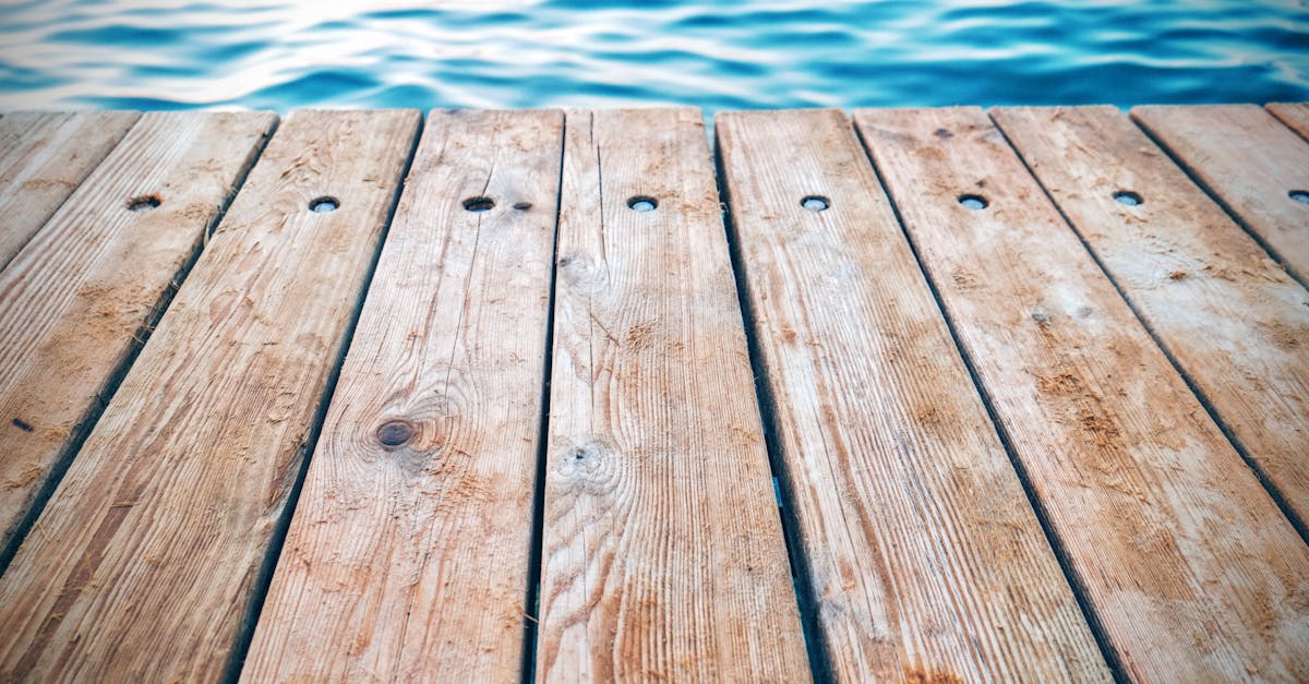 A detailed view of a rustic wooden pier with textured planks by calm blue water. Perfect for serene and nature themes.