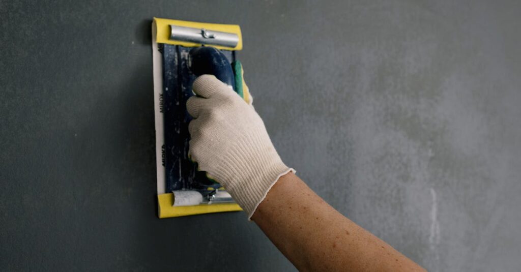Close-up of a hand smoothing a wall with a spackle tool during home renovation.